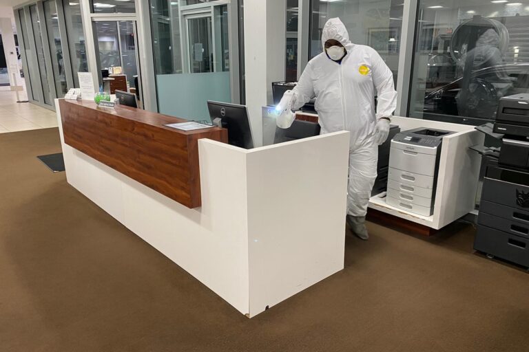 Man in hazmat suit spraying down desk