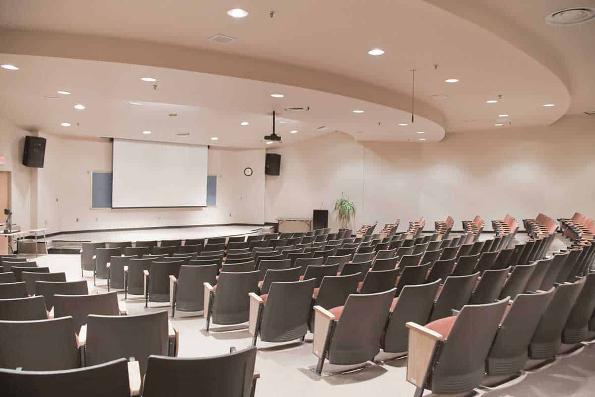 Interior of an auditorium with rows of chairs and a projector in the front.