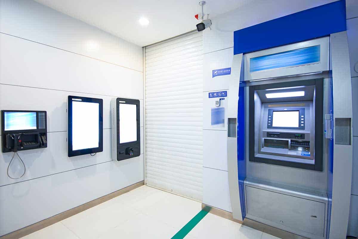 Indoor ATM bank machine with 3 screens on the wall next to it.