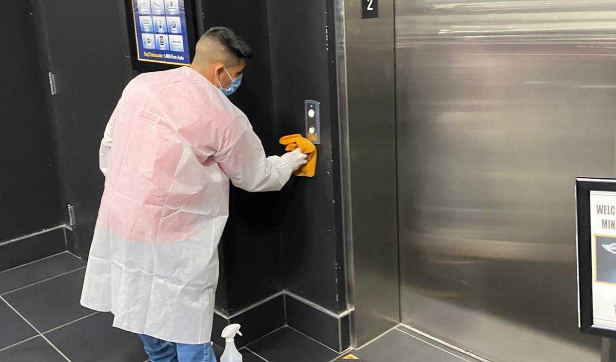 Man wearing cleaning equipment and cleaning the up and down buttons outside of an elevator.