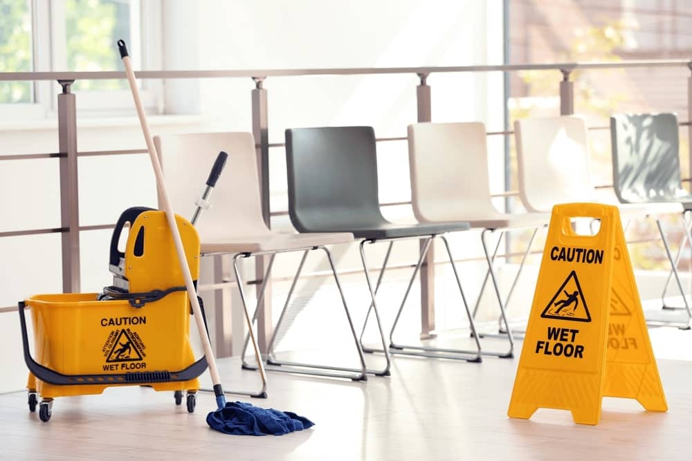 A wet floor sign next to a mop and other floor cleaning supplies in a facility