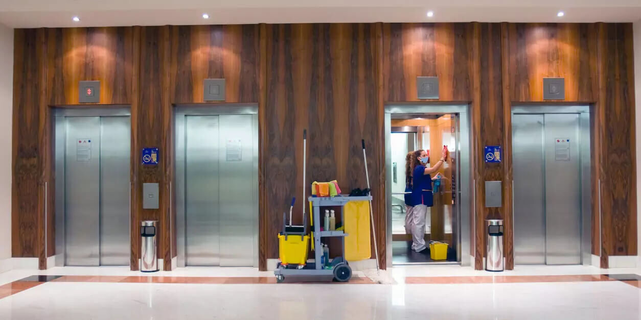 Woman cleaning the inside of an elevator in the lobby.
