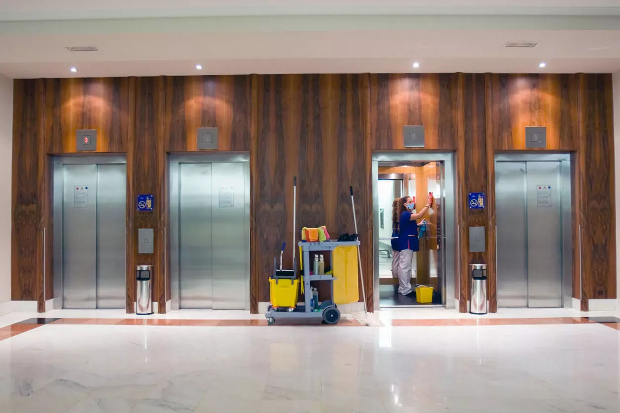 Woman cleaning the inside of an elevator in the lobby.