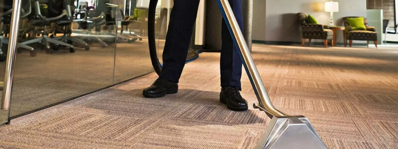 A worker using a cleaning tool to clean the carpets inside an office.