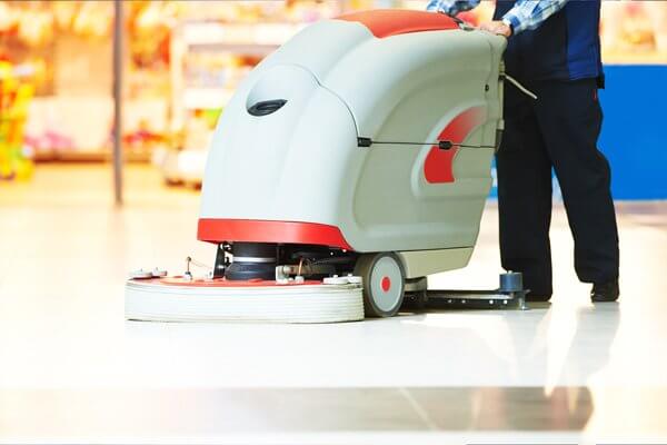 A worker using a large machine to clean the floors of a mall.