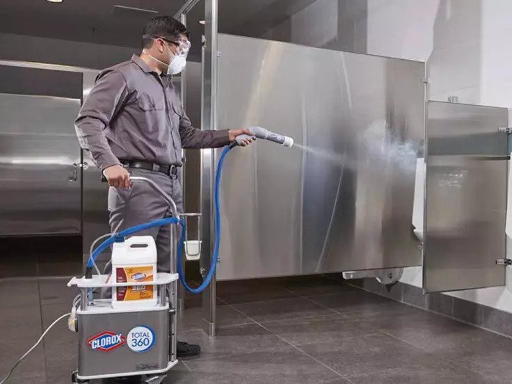 A worker using a spray cleaning tool to clean a public restroom.