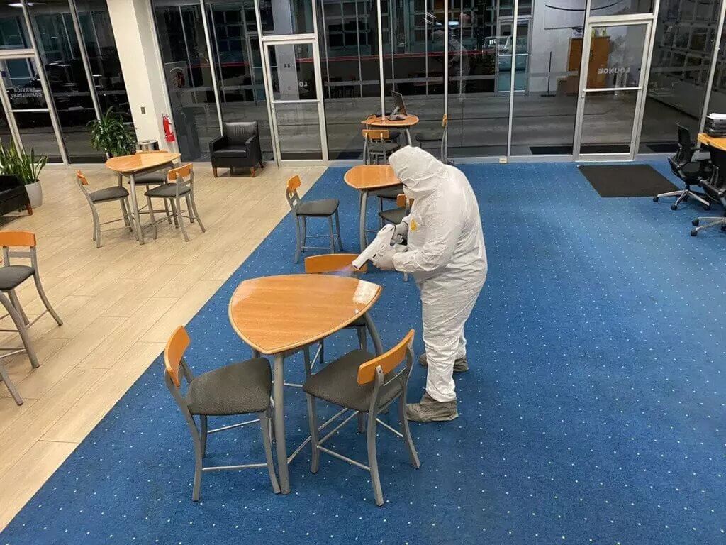 A sanitation worker using a spray gun to spray down a table inside an office lounge.