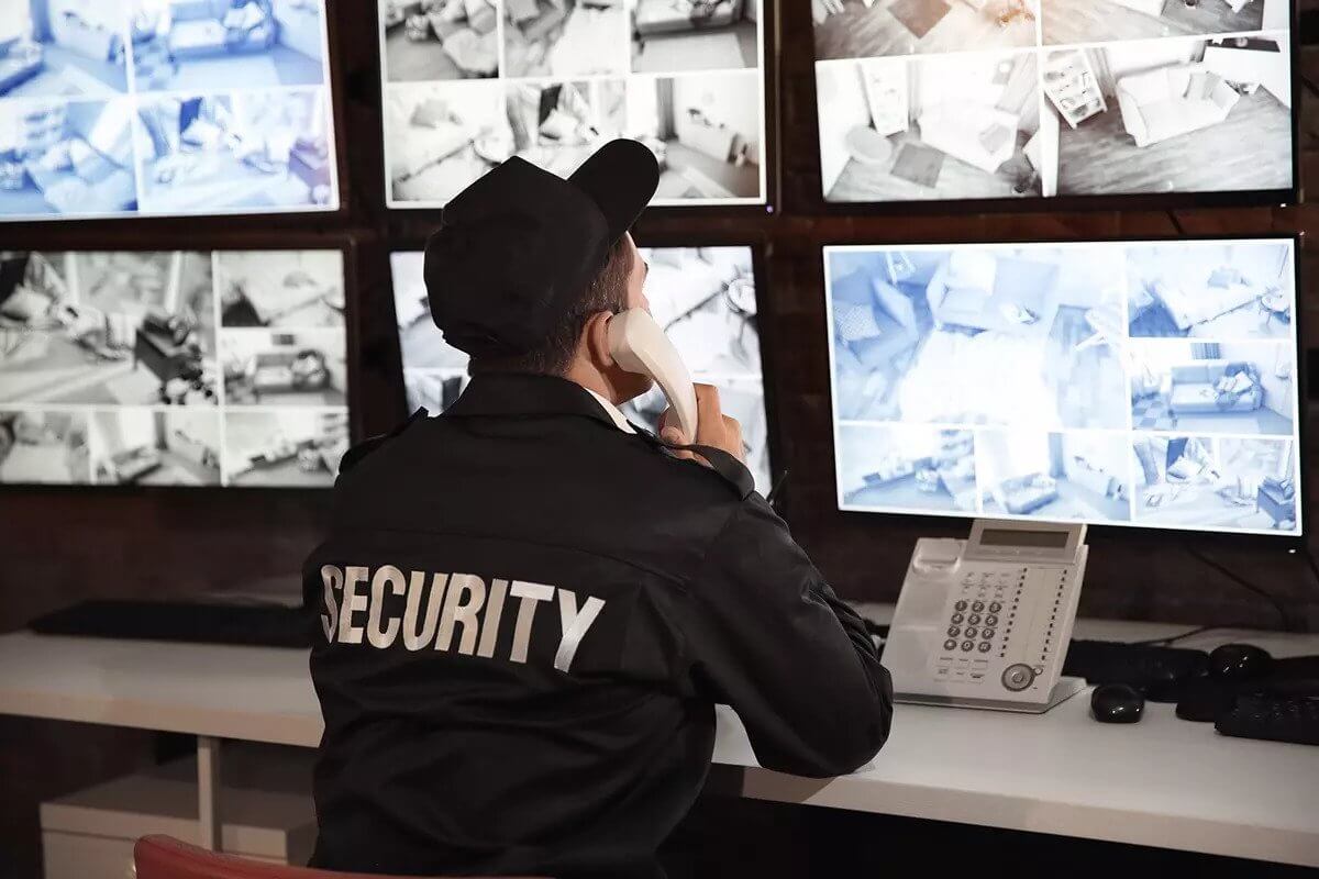 Security guard on the phone while looking at multiple screens.