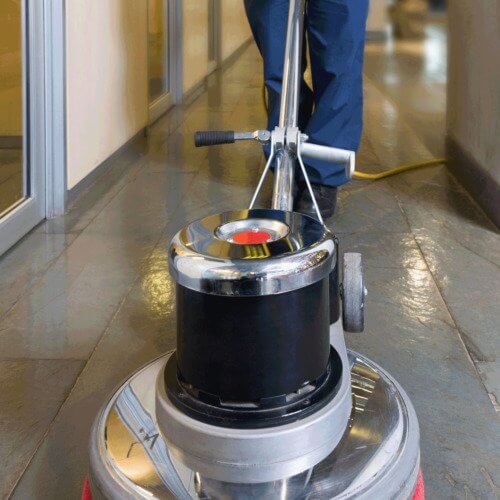 A worker cleaning the floors of inside a building with a floor scrubber.